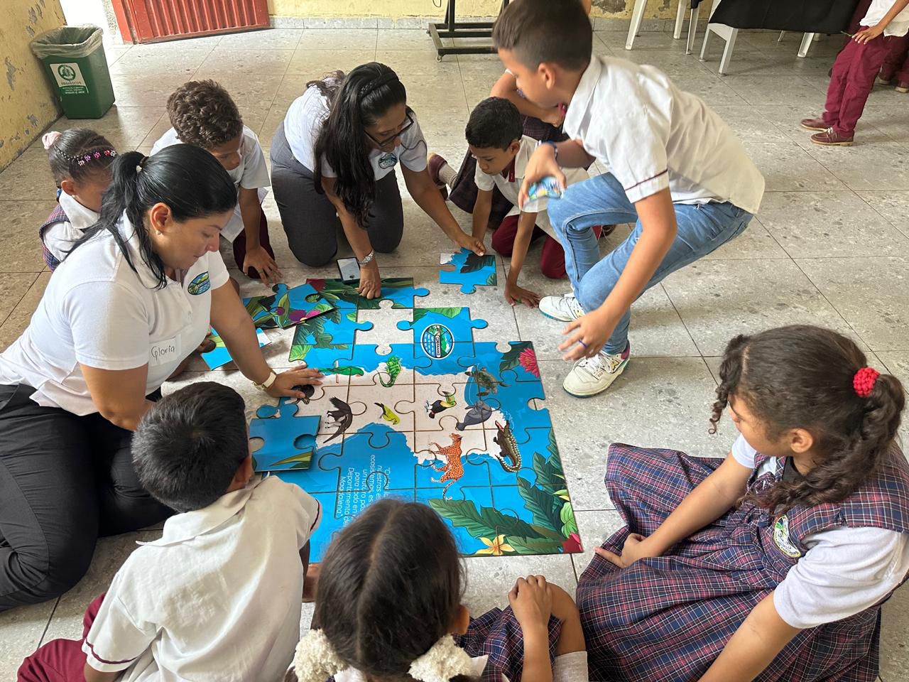 Funcionarias de CORPAMAG armando rompecabeza en el suelo con niños escuelas azules