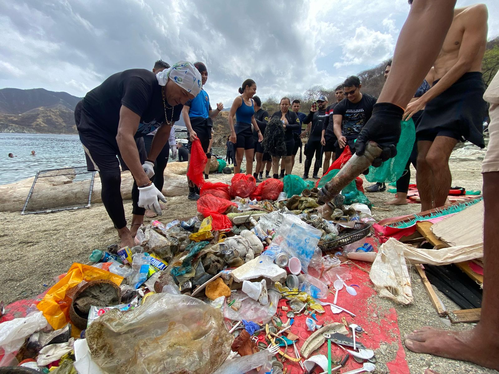 Grupo de personas junto a los residuos recogidos en la playa los cuales se encuetran en la arena