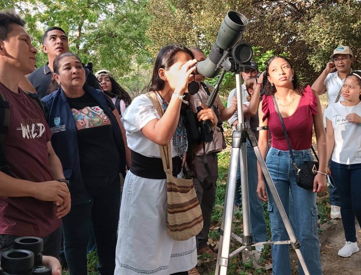 Consejera indigena de corpamag observando aves con binocular junto a otros participantes