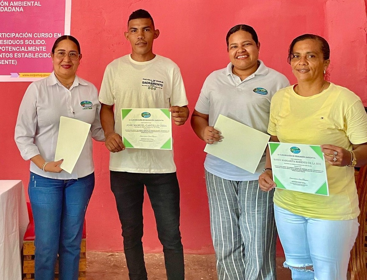 2 de los graduados junto a dos funcionarias sosteniendo diploma